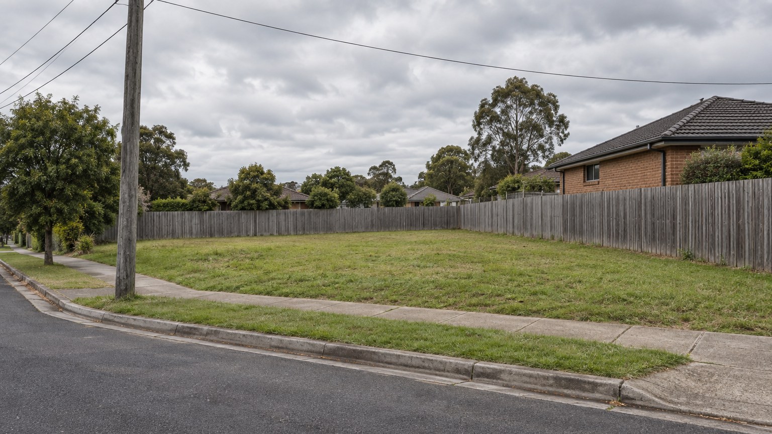 Empty grassed suburban corner lot with a street power pole at the boundary